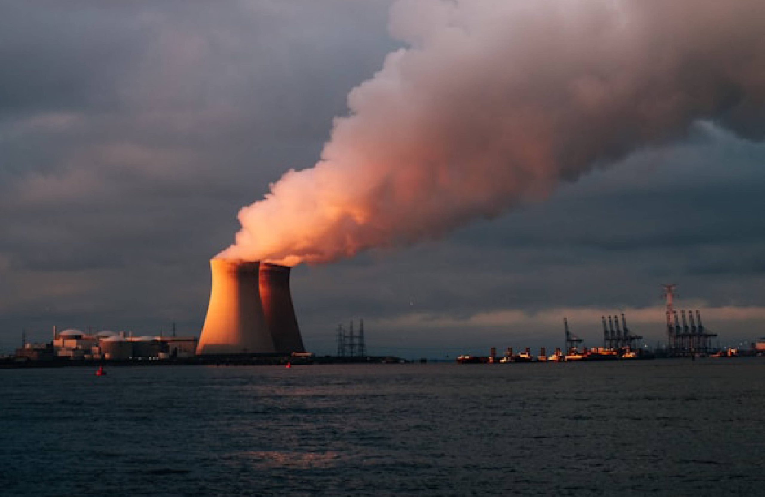 Nuclear power plant with steam and sunset sky by the water.