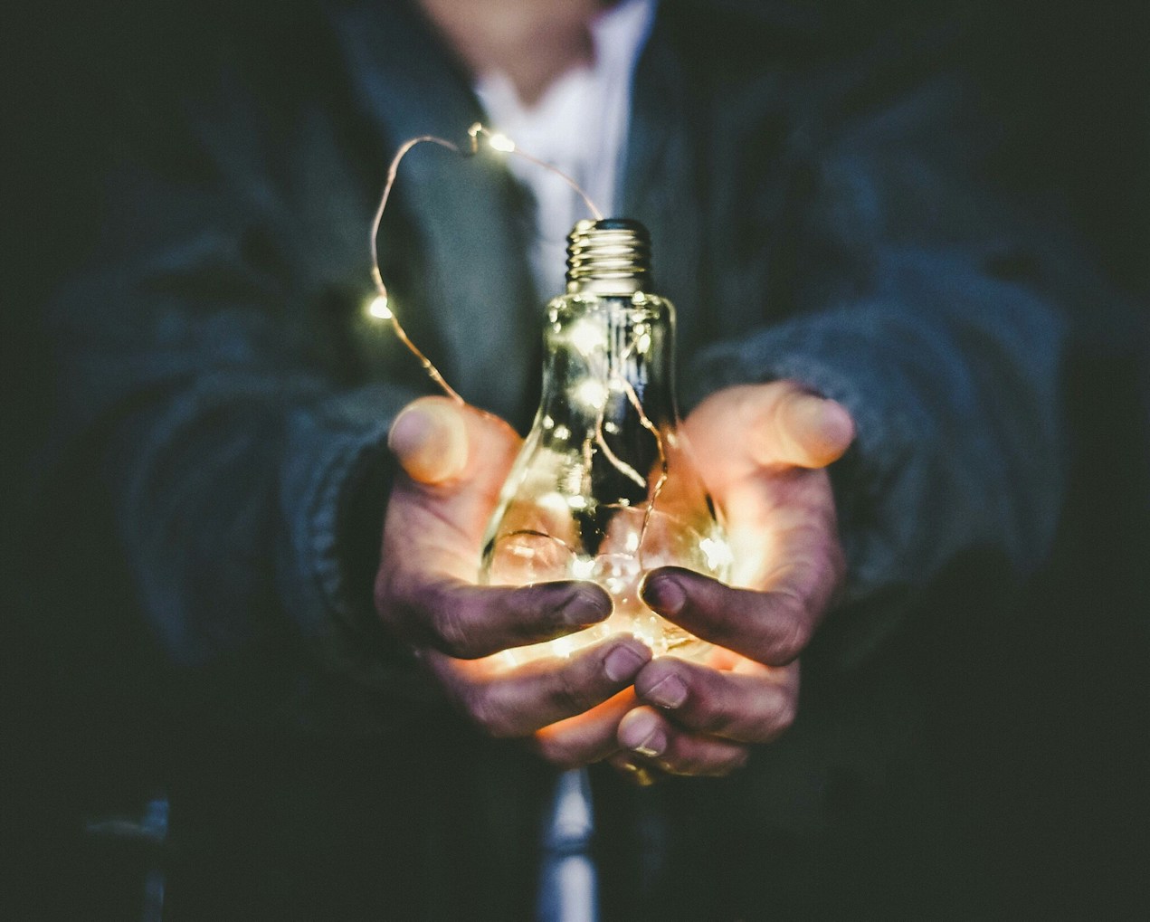 Hands holding a glowing light bulb with fairy lights inside.